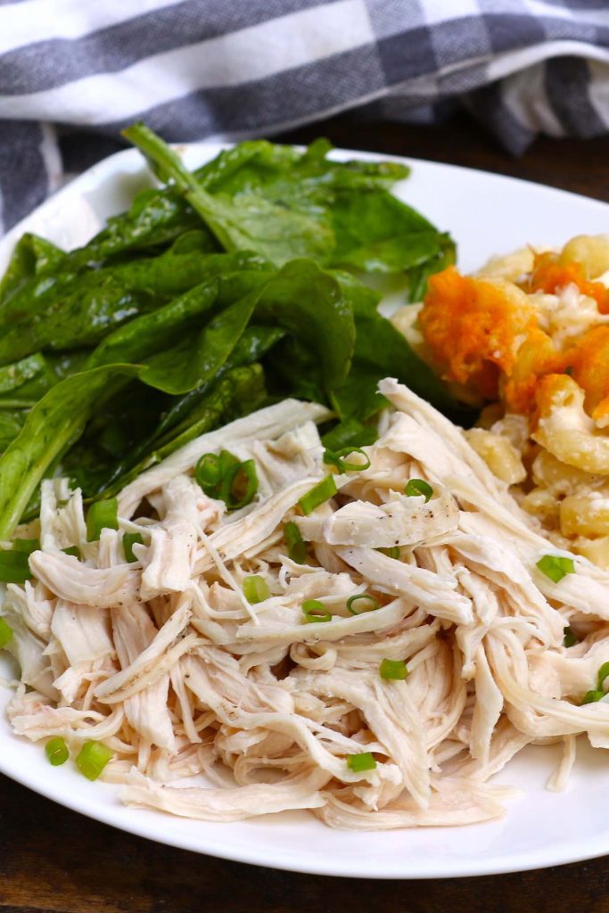 Pechugas de pollo cocidas al vacío desmenuzadas y servidas con verduras y pasta en un plato blanco.
