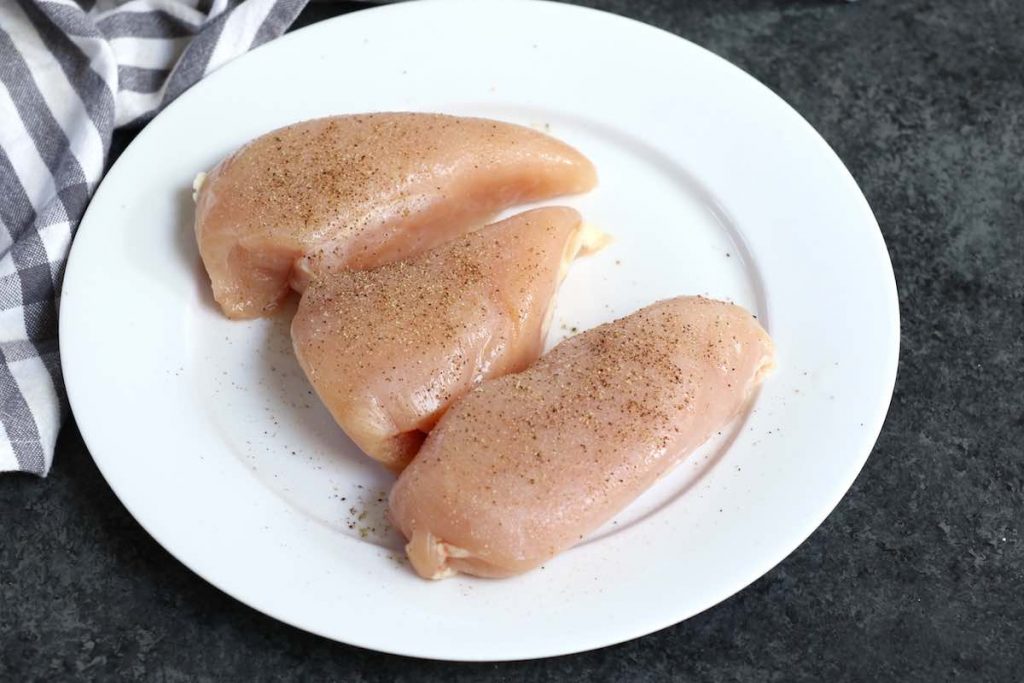 Pechugas de pollo crudas sazonadas con sal, pimienta y ajo en polvo en un plato blanco.