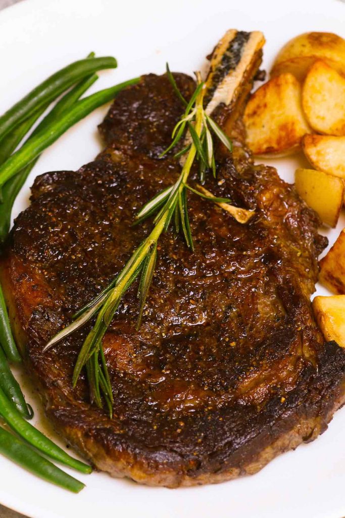 Chuletón cocido al vacío en un plato blanco y servido con judías verdes y patatas.