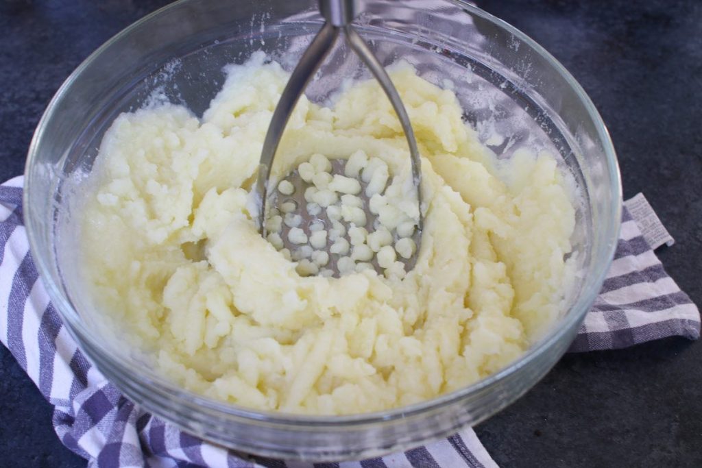 Triturar las patatas cocidas con un machacador de patatas.